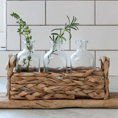 Straw basket with 3 glass bottles displayed with herb stems