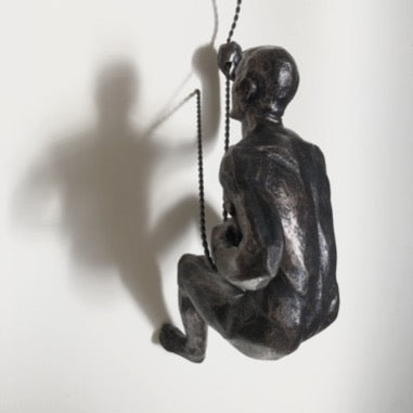 A antigiue bronze wall climbing man sculpture wall art hung on a twisted cord with loop top