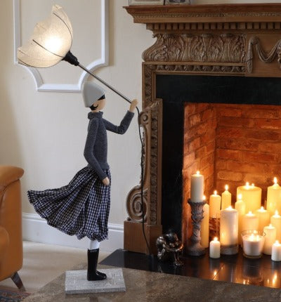 Iron Lady Lamp holding a grey shade, dressed in grey top and black & white flowing skirt